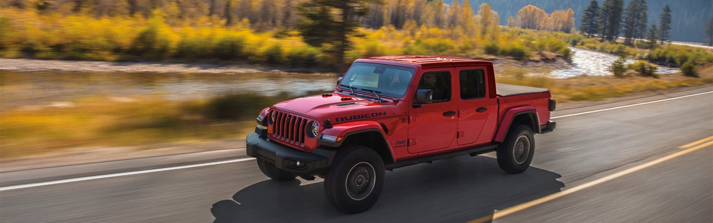 A 2021 Jeep Gladiator Rubicon being driven on a highway near grassy fields at sunset.