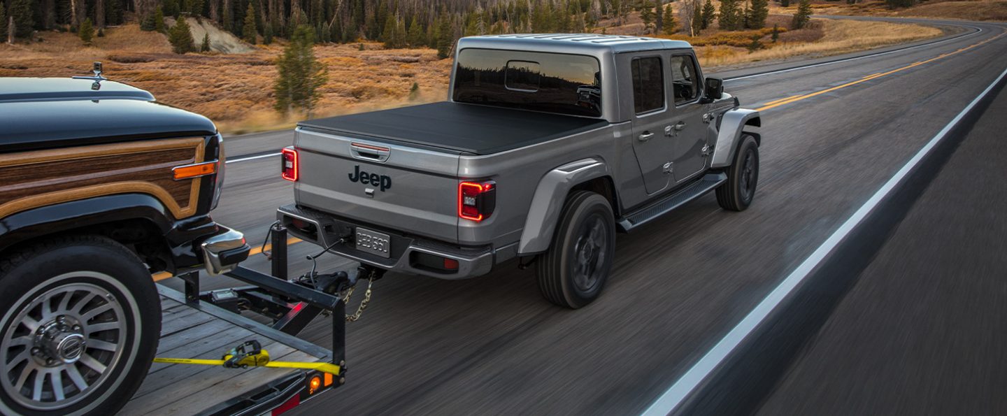 A 2021 Jeep Gladiator Overland towing a flatbed trailer with another vehicle on it.