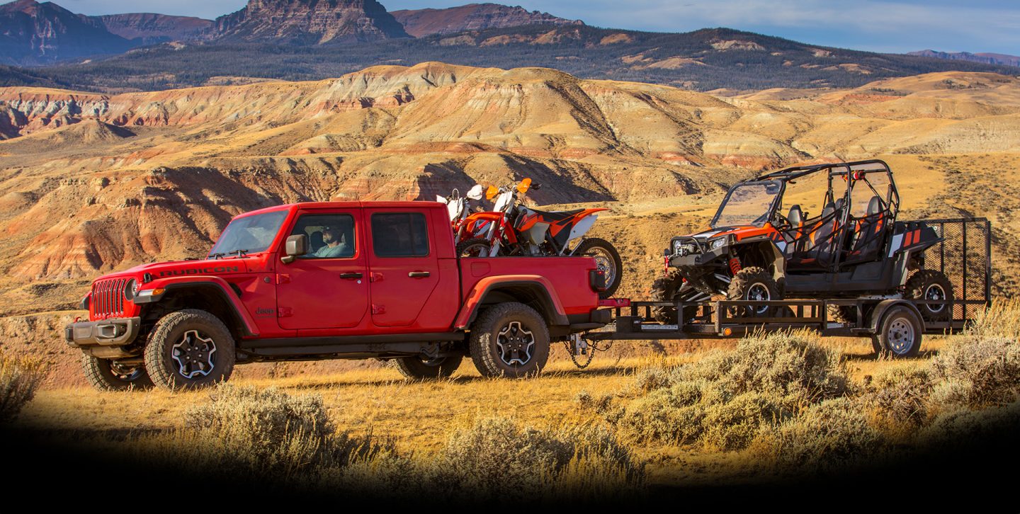 The 2022 Jeep Gladiator Rubicon with its doors off and windshield folded down, parked on a rocky beach.