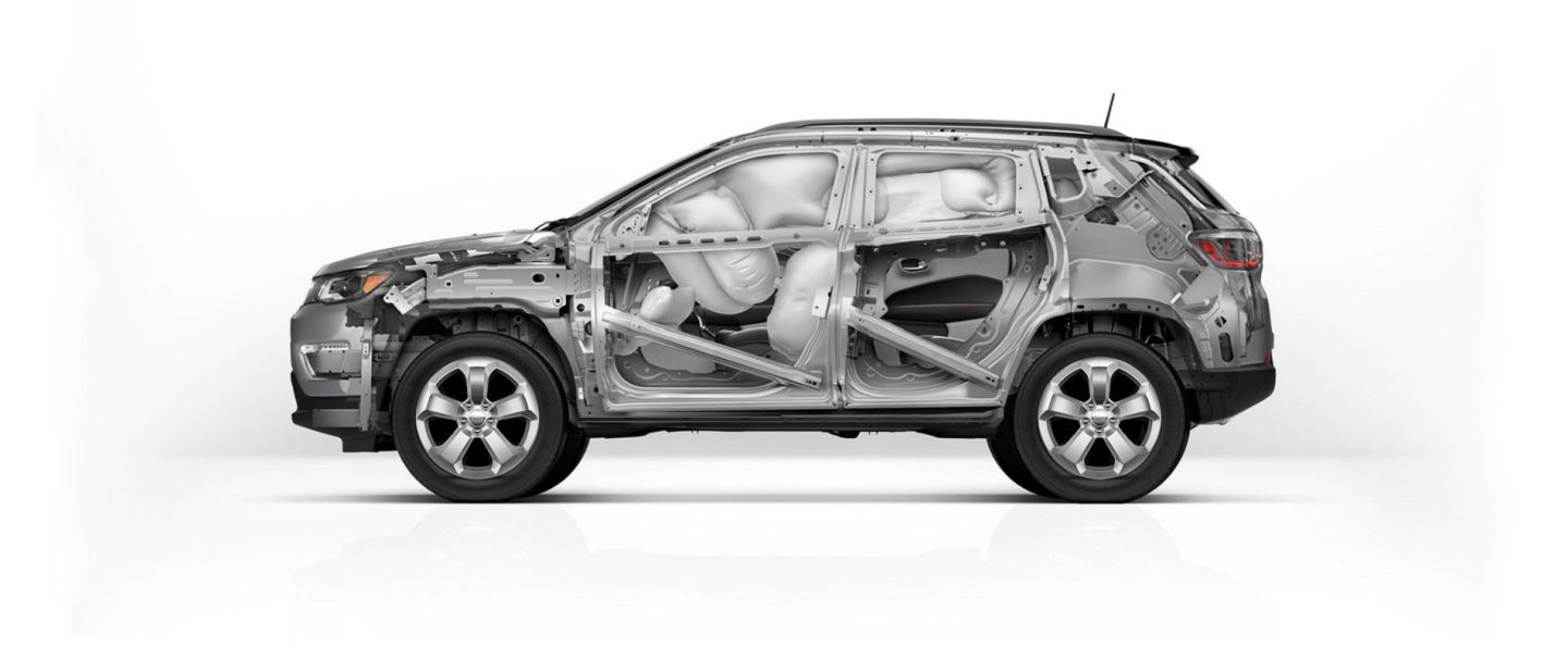 A 2021 Jeep Compass pulling away from a curb with its headlamps and fog lamps lit.