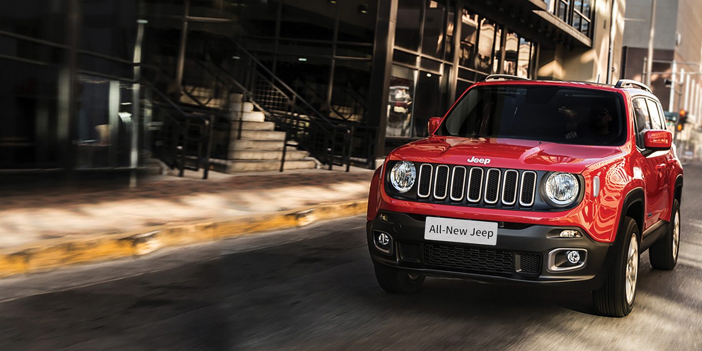 A three-quarter front view of a 2021 Jeep Renegade Latitude parked in front of a building with trees.